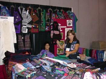 Chua Lee and her daughter arrange goods at their booth in the Global Marketplace. Their group, Fresno Interdenominational Refugee Ministries makes available Hmong cross stitch, reverse applique stitchery and other Southeast Asian refugee crafts.