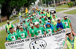 A group of marchers in green t-shirts, holding a white sign.