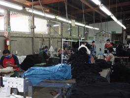 People wearing masks while working with sewing machines in a warehouse environment.